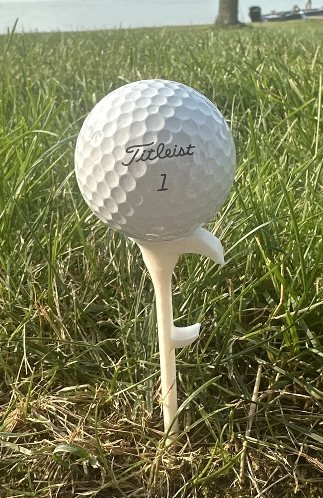 Real Shotgun Start Tee holding a golf ball in the grass by the water